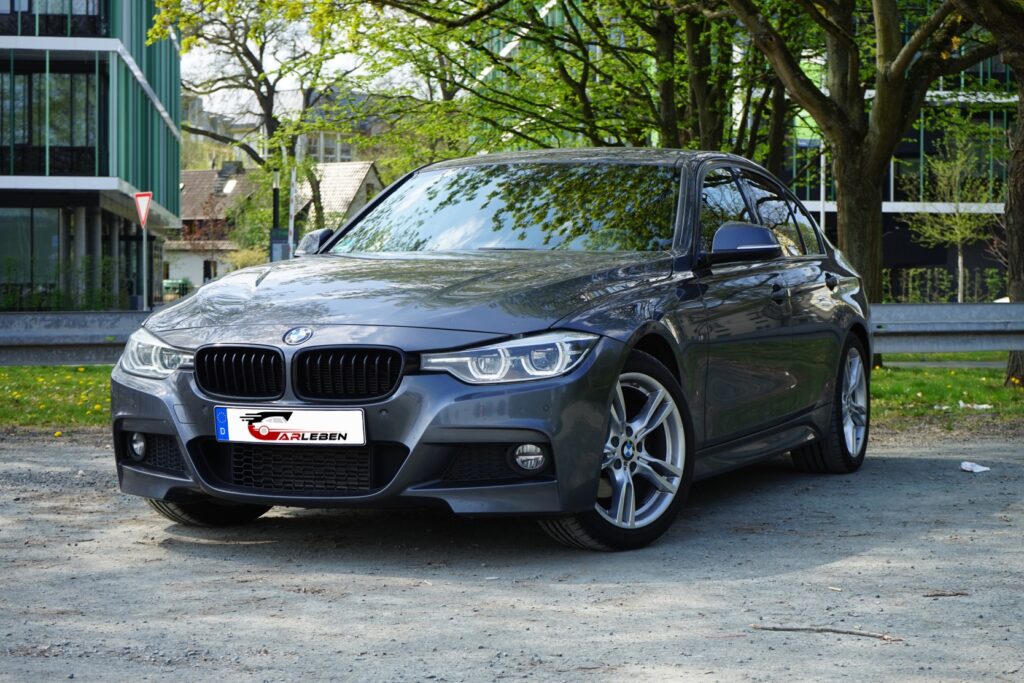 Grauer BMW 3er-Limousine, geparkt auf einem Schotterplatz in Herborn mit Carleben Kennzeichen, im Hintergrund moderne Gebäude und Bäume.